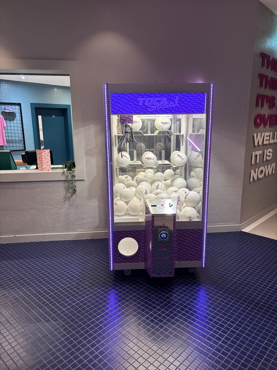 Claw machine prize grabber with purple LED border filled with white soccer balls behind glass.