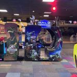 Large 'GAMES AREA' sign above an arcade with racing game machines and science-fiction graphics; colorful tiled floor.